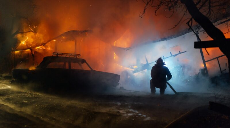 Pompier éteignant avec le tuyau l'incendie de la maison et de la voiture lors d'un accident de nuit