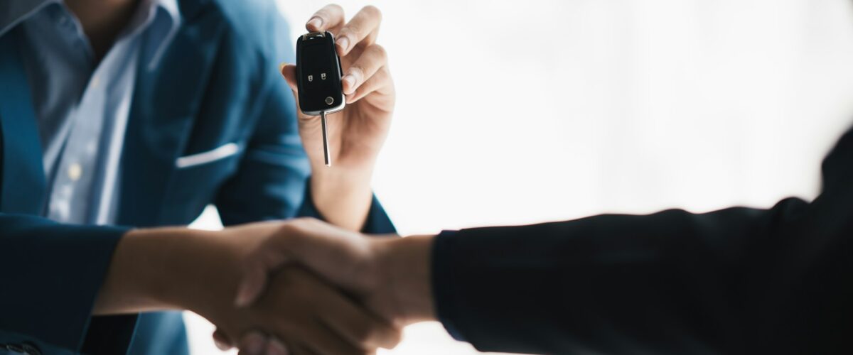 L'agent commercial et le client se serrent la main, donnant la clé automatique du véhicule au client une fois la transaction conclue avec succès.