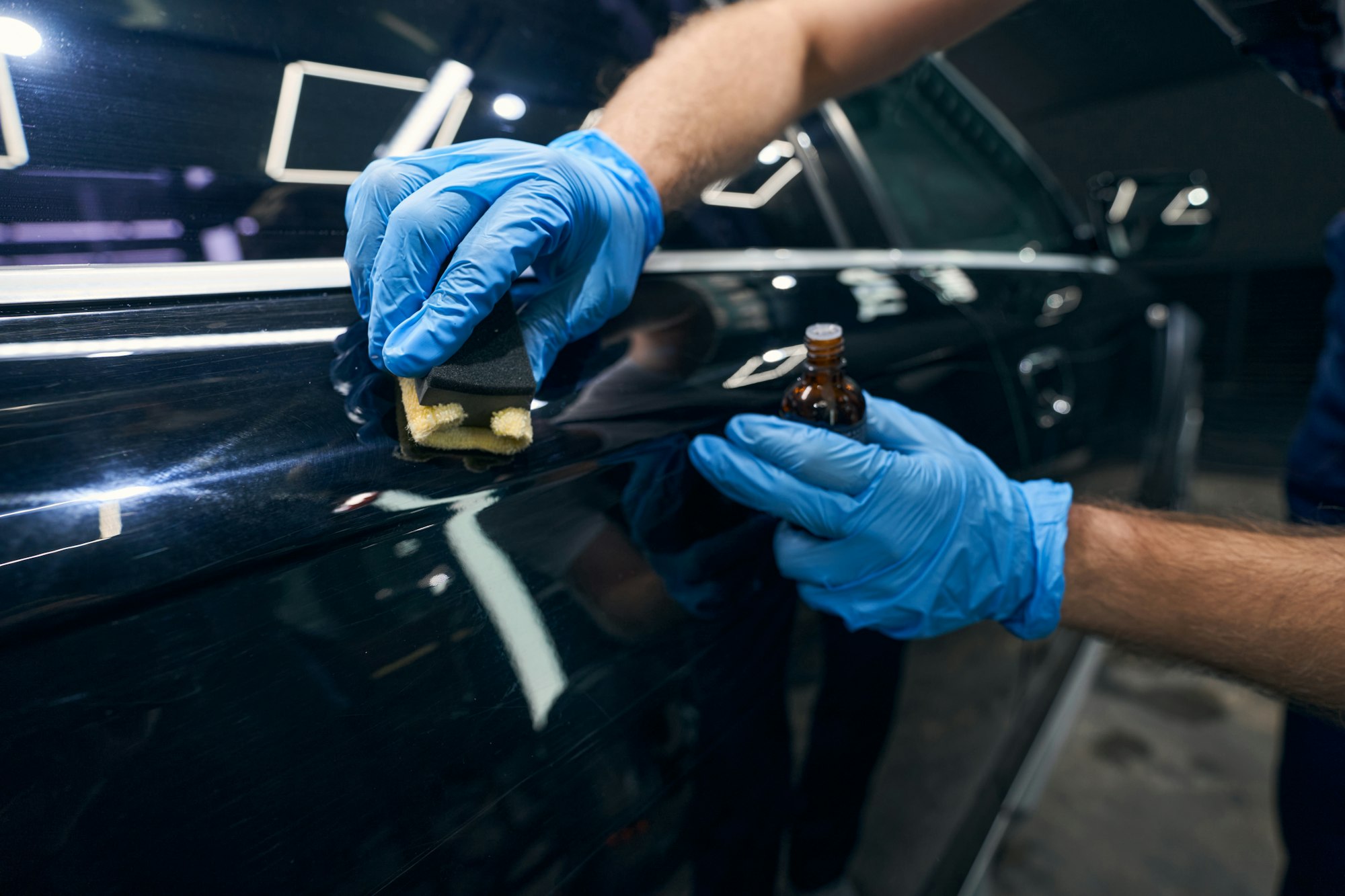 Mécanicien réparant les rayures et les imperfections de la surface de l'automobile avec un revêtement en céramique et un applicateur en microfibre