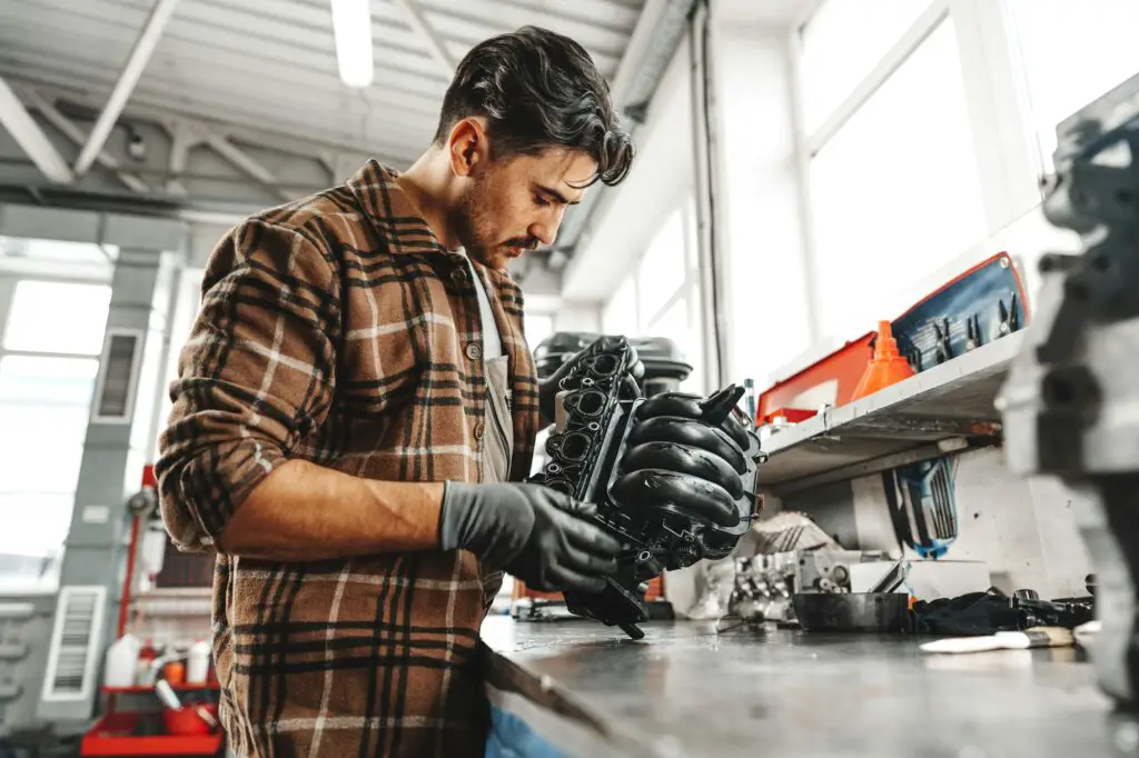 Jeune homme mécanicien réparant des pièces de voiture sur une table de travail dans un atelier de service automobile en gros plan