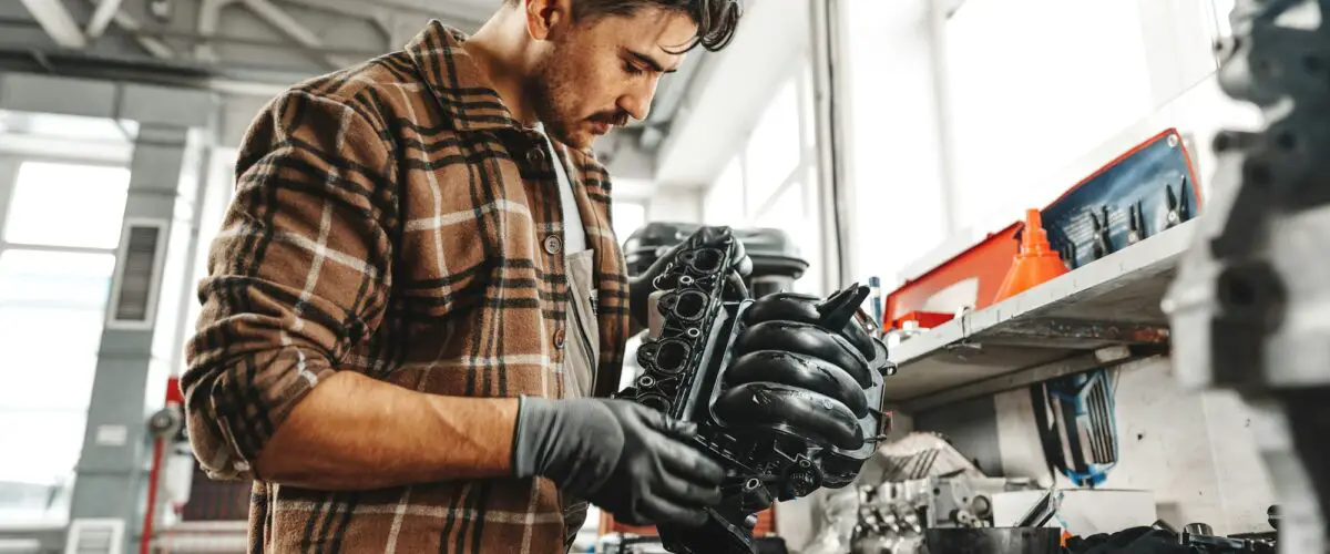 Jeune homme mécanicien réparant des pièces de voiture sur une table de travail dans un atelier de service automobile en gros plan