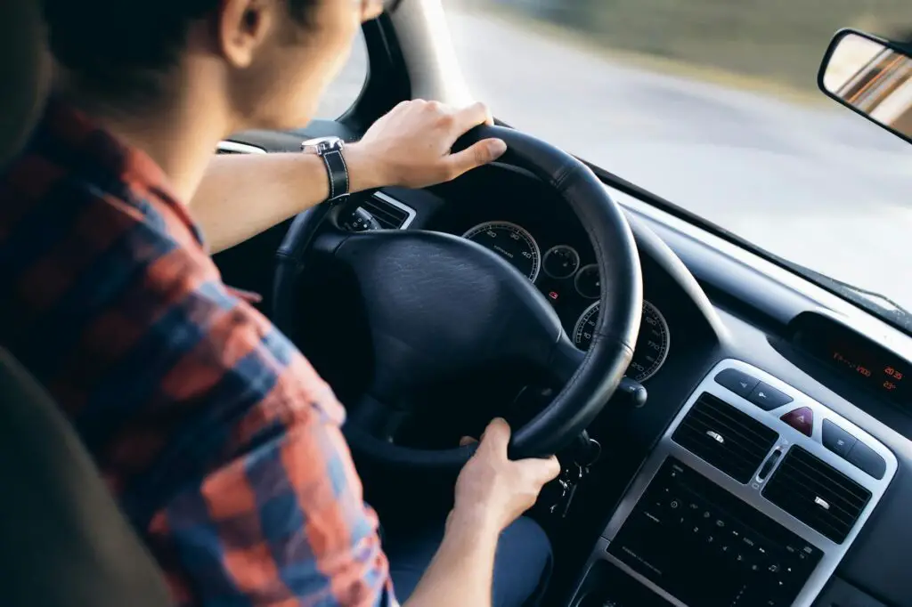 Vue rapprochée d'un homme conduisant une voiture moderne, montrant le tableau de bord et les détails de direction.