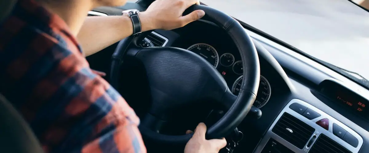Vue rapprochée d'un homme conduisant une voiture moderne, montrant le tableau de bord et les détails de direction.