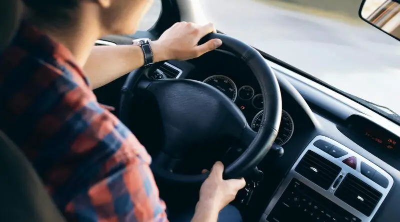 Vue rapprochée d'un homme conduisant une voiture moderne, montrant le tableau de bord et les détails de direction.