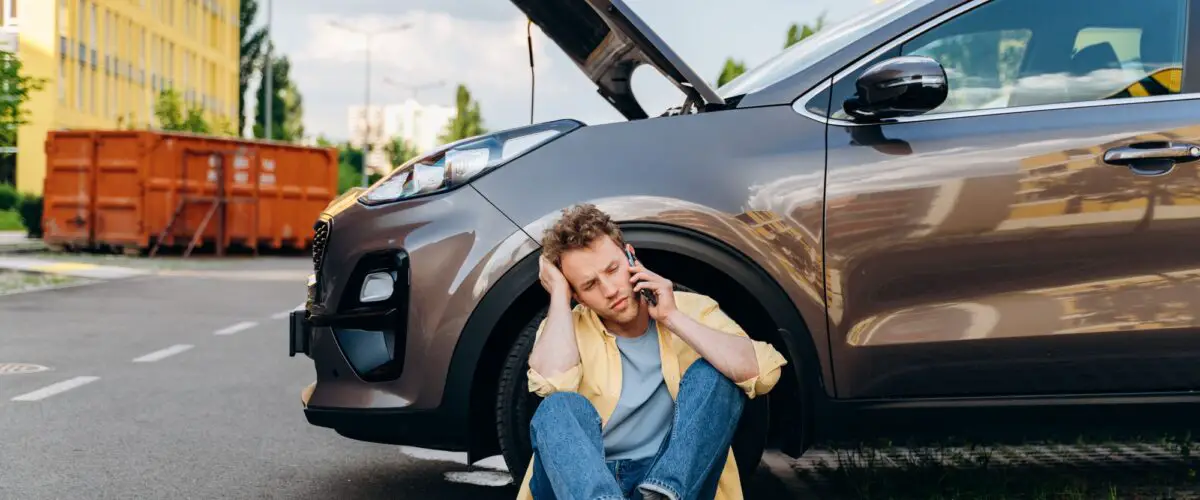 Jeune homme utilisant un téléphone portable près d'une voiture cassée dans la ville.