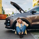 Jeune homme utilisant un téléphone portable près d'une voiture cassée dans la ville.