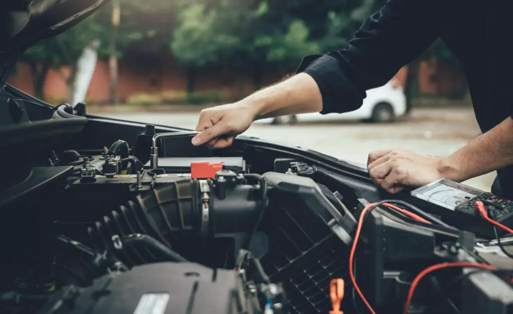 Le mécanicien de voiture vérifie le moteur et maintient la jauge de batterie.