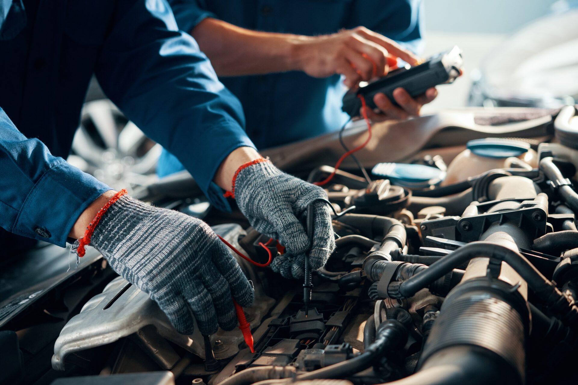 Image en gros plan des gants de protection mécaniciens lors de l'utilisation du multimètre pour tester la batterie automobile