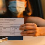 White Woman in Face Mask montrant une carte de disques de vaccination tandis que vous êtes assis en voiture