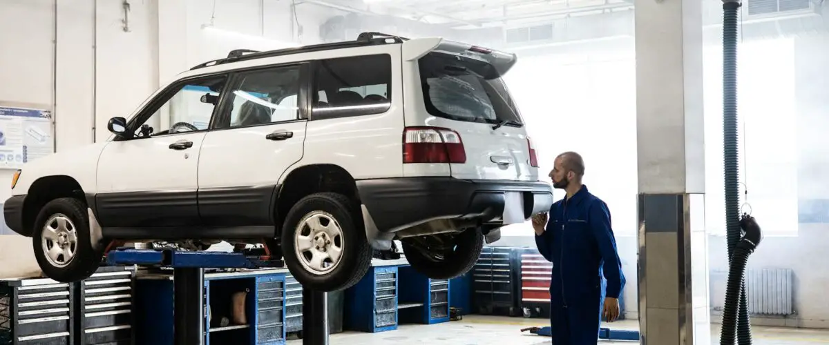 Mécanique inspectant un SUV levé dans un garage de réparation automobile moderne.