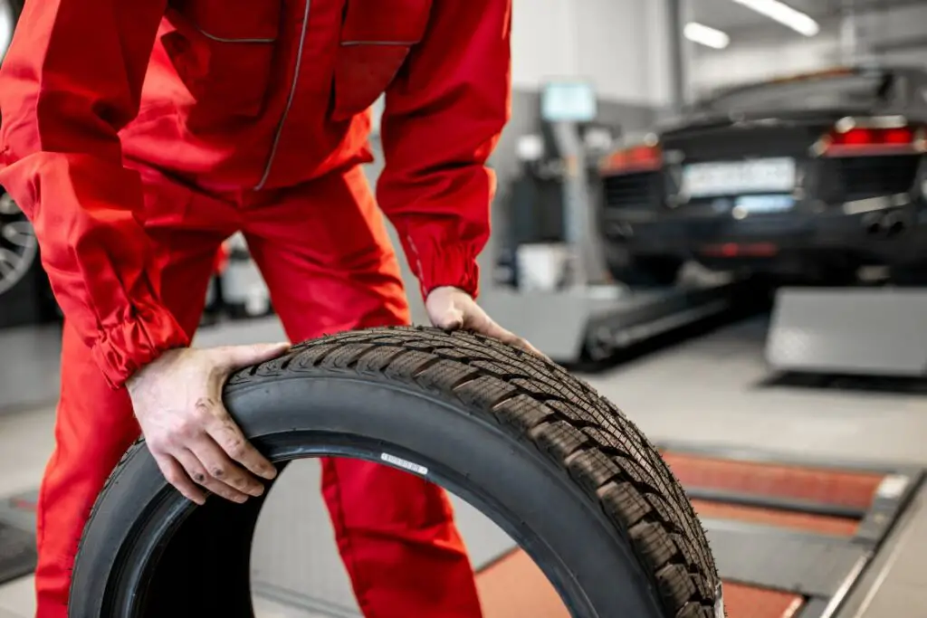 Travailleur en uniforme transportant de nouveaux pneus au service ou en magasin, vue grossière