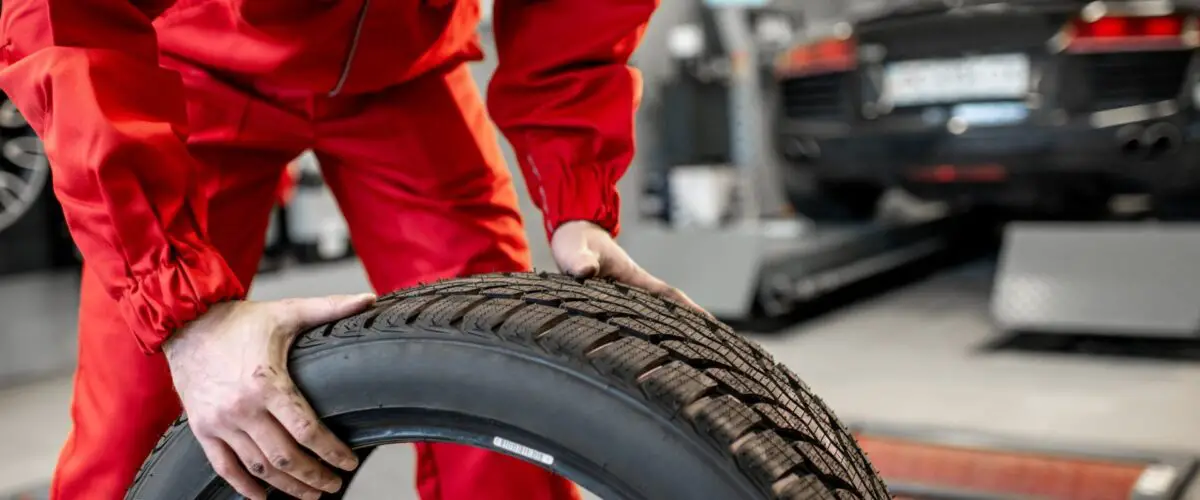 Travailleur en uniforme transportant de nouveaux pneus au service ou en magasin, vue grossière