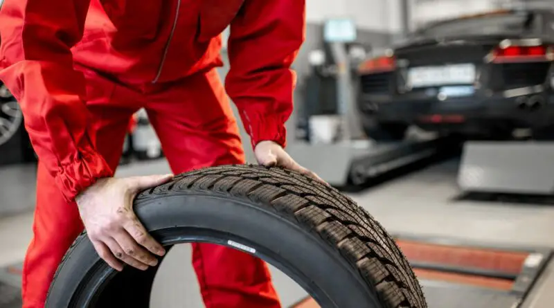 Travailleur en uniforme transportant de nouveaux pneus au service ou en magasin, vue grossière