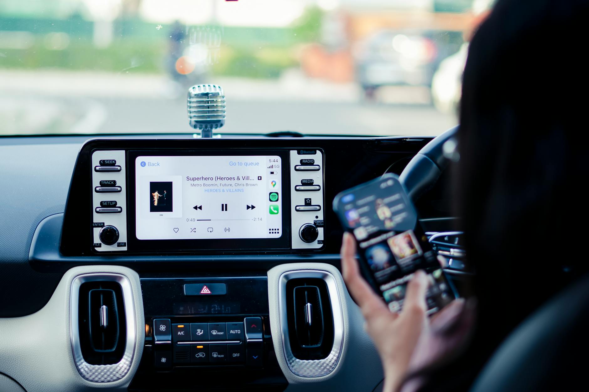 Tableau de bord de voiture avec écran tactile et personne utilisant un smartphone à l'intérieur d'un véhicule.